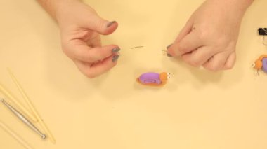 Bayan bej masadaki yumuşak polimer kilden salyangoza küçük siyah filizler takıyor.