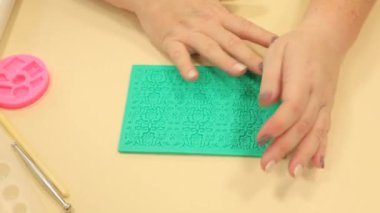 Kadın yeşil silikon küf koyarak merdaneli pembe polimer kil çıkarıyor.