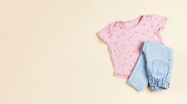 Çocuk pembe tişörtü ve bej arka planda katlanmış kot pantolon. Bir kız için modaya uygun bir görünüm. Düz yatıyordu. Pankart