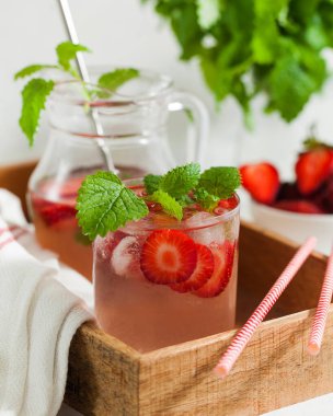 Ev yapımı taze çilekli limonata ya da naneli kokteyl, sürahide buz küpleri ve arka planda ahşap tepside duran cam.