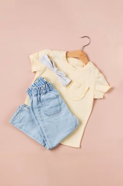 Pembe arka planda sarı tişörtlü, kot pantolonlu çocuksu bir imaj. Düz yatıyordu.