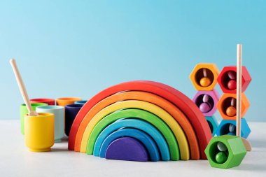 Beyaz masa üzerinde gelişen küçük çocuklar için basit tahta oyuncaklar. Kreşteki gökkuşağı bardakları ve inşaat küpleri. Bebek büyütme ve öğrenim