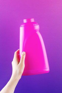 Kadının elinde mor arka planda boş mor bir şişe beyazlatıcı var. Temizlik için organik ürün. Tasarım için boşluk