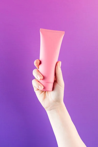 Mockup of a pink tube with a cosmetic product on a purple background. Copy space.