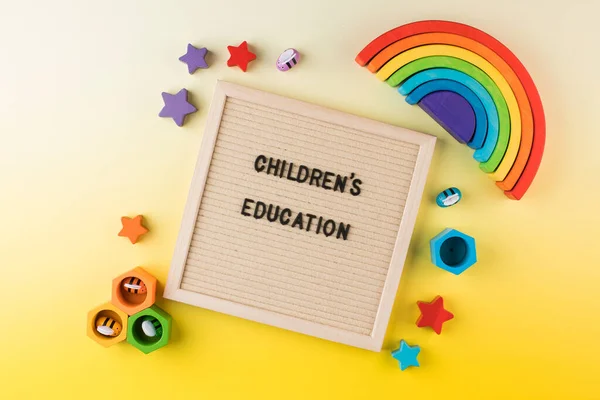 A frame with the words CHILDRENS EDUCATION surrounded by educational bright wooden toys on a yellow background.