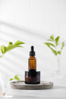  Kahverengi krema kavanozu ve yeşil bitki ve gölgelerin arka planına karşı doğal bileşimi olan yüz derisi için serum içeren bir damlatıcı..