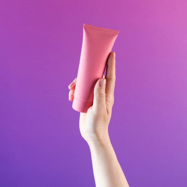 Mor arka planda kozmetik ürünü olan pembe bir tüp. Boşluğu kopyala. 