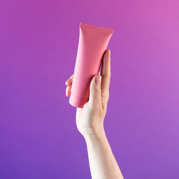 Mockup of a pink tube with a cosmetic product on a purple background. Copy space.