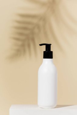 Sarı arka planda içi boş doldurulabilir şeker şişesi ve yakın plan palmiye yaprağı gölgesi. Yaz tatilinde cilt bakımı. Boşluğu kopyala