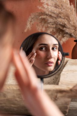  Genç bir esmer kadın aynaya yansıyor gözlerinin altında hidrojel pembe yamalar var. Güzellik, kendine bakım, kozmetik, gençlik kavramı..