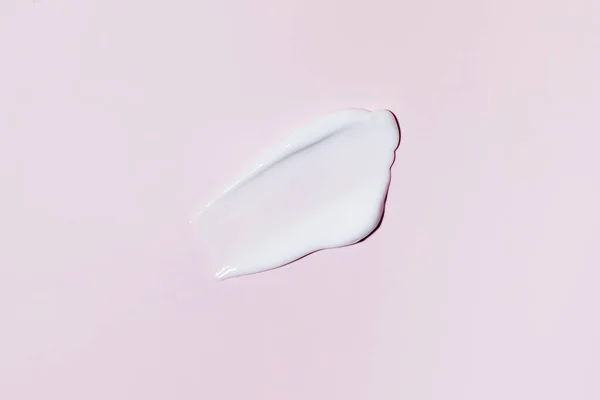 White cosmetic smear on a pink background, nourishing cream. A sample for advertising.