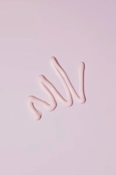 A smear of pink cosmetics on a pink background. A sample for advertising, a skin care concept. Copy space