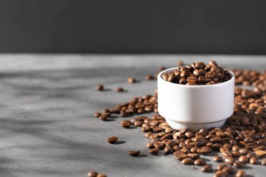 Beyaz bardakta kavrulmuş kahve çekirdekleri, etrafa saçılmış kahve çekirdekleri. Kafe konsepti, kafe..