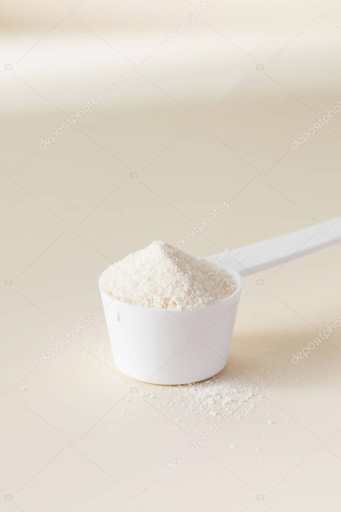 A scoop with hydrolyzed collagen powder on a beige background. The concept of food additives, healthy.