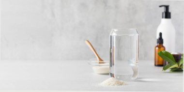 Bir bardak su, gri arka planda bir bardak kolajen tozu ve bakım kozmetiği. Yaşlanma karşıtı prosedürler, sağlıklı beslenmek için besin takviyeleri. Boşluğu kopyala