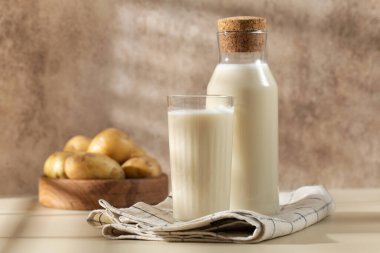 Bir bardak ve bir sürahi patates sütü ve içinde çiğ patates var. Süt ikamesi, vejetaryenler için süt. 
