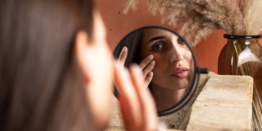 Makyaj masasında göz altı bandı takan bir kadının yansıması. Profesyonel yüz bakımı. Antiaging ve ferahlatıcı kozmetik ürünler