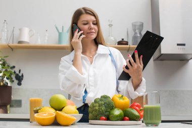Diyetisyen, hastaya telefonla tavsiye veriyor. Nutrakötik mutfakta taze meyve ve sebzelerle birlikte. Sağlık hizmetleri