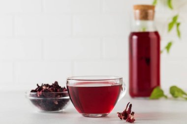 Hafif arkaplanda şeffaf bir fincanda bulunan amber yaprağından yapılmış bitki çayı ve bir kase kuru amber çiçeği..