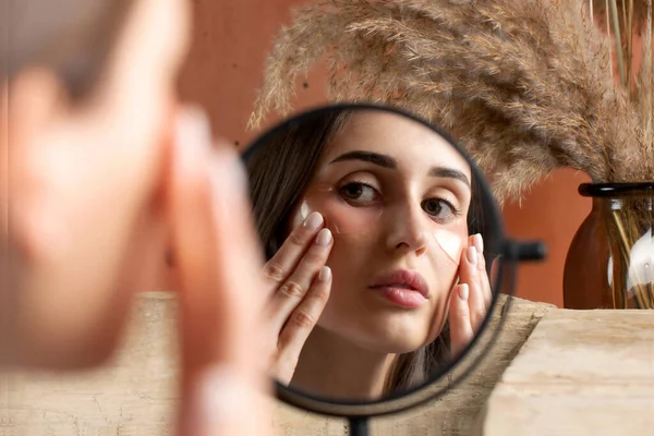 Reflection of woman applying under-eye patch at dressing table closeup. Professional facial skin care. Antiaging and refreshing cosmetic products. Banner