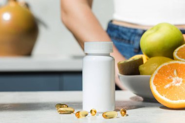  Mutfak masasında D vitamini ya da balık yağı kapsülleri olan beyaz plastik bir kavanoz. Sağlıklı yaşam tarzı, besin takviyeleri.