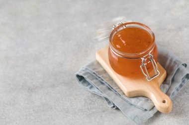 Gri beton arka planda meyveli turuncu reçelli cam kavanoz. Meyve koruma. Boşluğu kopyala.