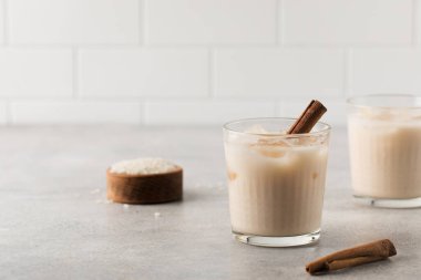 Ev yapımı Horchata pirinç, gri beton arka planda buzlu ve tarçın çubuklu bir bardakta içilir. Vejetaryen meşrubatı, ulusal mutfak. Boşluğu kopyala.