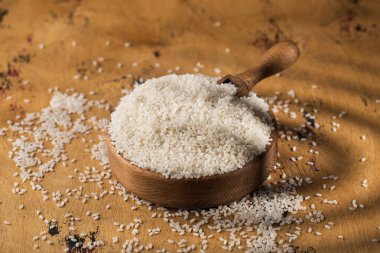 Tahta bir kasede çiğ beyaz pirinç ve ahşap bir arka planda tahta bir kaşıkta. Vejetaryen yemeği. Sağlıklı yemek..