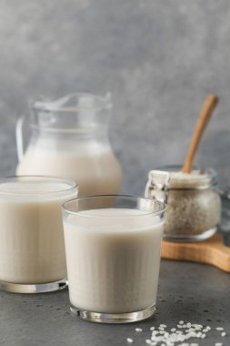 Bir bardak sebzeli pirinç sütü ve gri arka planda bir sürahi. Vejetaryen yemeği, laktozsuz süt. Sağlıklı yaşam tarzı.