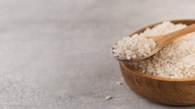 Tahta bir kasede çiğ beyaz pirinç ve gri bir arka planda tahta bir kaşıkta. Vejetaryen yemeği. Sağlıklı yemek..