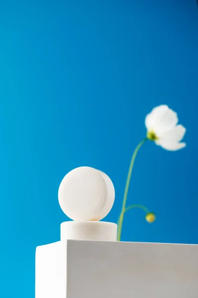 Round soap on a white podium on a blue background with a white flower. Hygiene products.