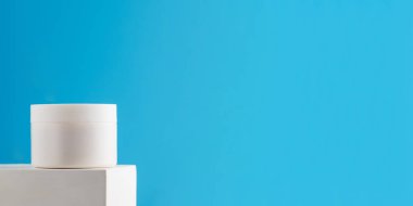 Beyaz bir kavanozun maketi, besleyici bir yüz ve vücut kremi ile mavi arka planda bir kaide. Cilt bakımı. Boşluğu kopyala