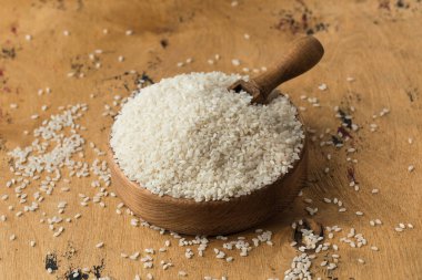 Tahta bir kasede çiğ beyaz pirinç ve ahşap bir arka planda tahta bir kaşıkta. Vejetaryen yemeği. Sağlıklı yemek..