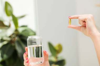Bir kadın elinde D vitamini ya da Omega-3 vitamini içeren sarı şeffaf bir kapsül tutar. Sağlıklı yaşam tarzı, önleyici tıp kavramı.