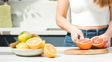  Bir kadın mutfaktaki masada greyfurt kesiyor, taze meyveli bir tabak. Sağlıklı gıda konsepti. Vejetaryenlik.