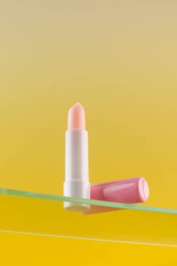  Sarı arka planda cam bir raftaki pembe nemlendirici ruj. Cilt bakımı kavramı.