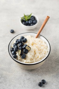 Pirinç sütlü yaban mersinli yulaf lapası ve gri arka planda yakın plan bir kasede. Sağlıklı ve lezzetli kahvaltı konsepti.