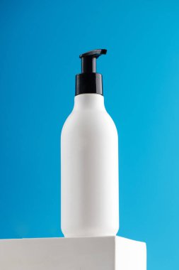 Kozmetik ürünü olan beyaz bir dağıtıcının maketi. Mavi arka plandaki bir podyumda logonuz için yer var..