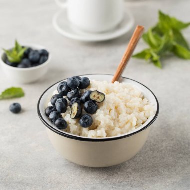 Pirinç sütlü yaban mersinli yulaf lapası ve gri arka planda yakın plan bir kasede. Sağlıklı ve lezzetli kahvaltı konsepti.