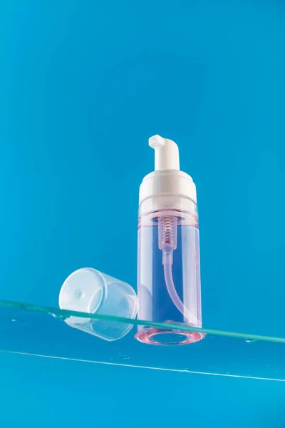 Dispenser mockup with face wash foam on a glass shelf on a blue background. Acne remover, makeup remover. Skin care.