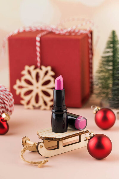 Pink lipstick on a wooden sled on a New Years background. Stylish Christmas lipstick advertisement. A New Years gift for a woman.