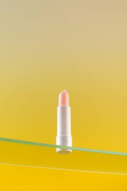  Sarı arka planda cam bir raftaki pembe nemlendirici ruj. Cilt bakımı kavramı.