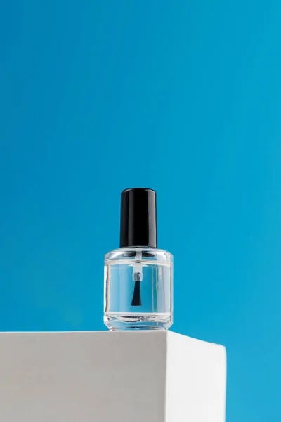 Transparent nail polish stands on a podium on a blue background. Copy space