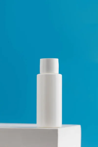 White tube with a cosmetic product on a podium on a blue background. The concept of natural plant cosmetics. Layout.