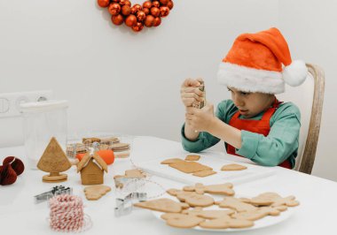 Yakışıklı bir çocuk Noel Baba şapkasıyla Noel Baba 'nın masasında zencefilli kurabiye süslüyor. Çocuklarla Noel tatili.