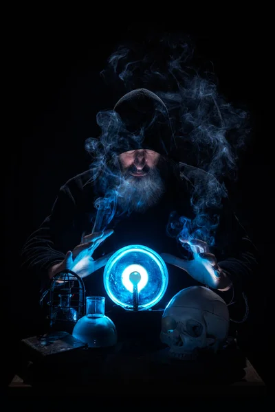 Hexenmeister erraten die Zukunft mit einer blauen Kristallkugel, umgeben von Rauch, Büchern, einem Totenkopf und mystischen Elementen. — Stockfoto