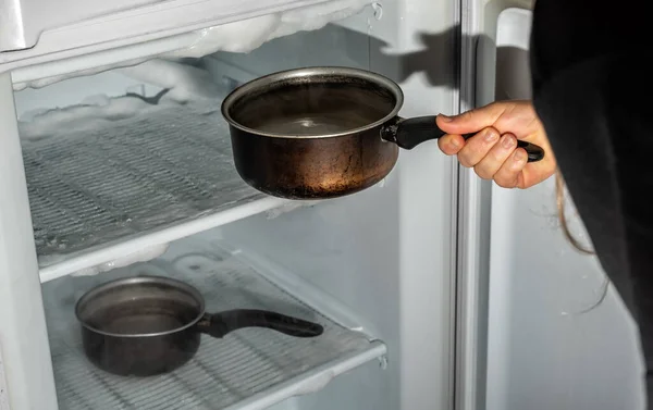Melting the ice from the freezer with the help of saucepans with hot water. — Stock Photo, Image