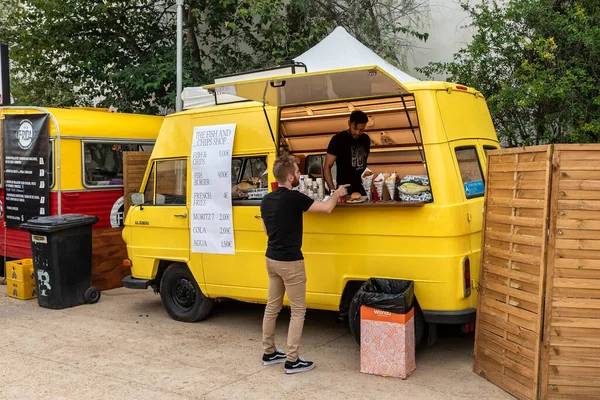 SİTGES, BARCELONA, İSPA - 08 Ekim 2022: Sarı retro minibüs caddede fast food satmaya hazır ve müşteri cips ve balık siparişi veriyor