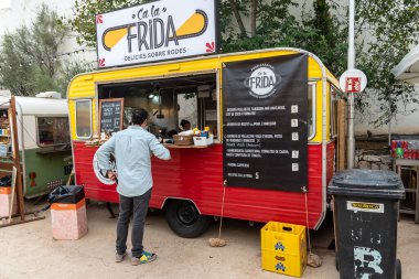 Sitges, Barcelona, İspanya - 08 Ekim 2022: Sokaklarda fast food satışına adapte olmuş bir karavanda hizmet bekleyen müşteri