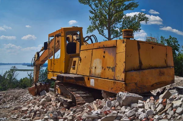 Vieja excavadora sobre las ruinas de una antigua casa . —  Fotos de Stock